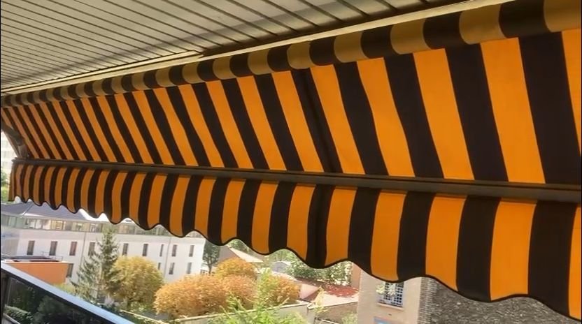 Store banne a toile rayee orange et noire pose sur un balcon d appartement en Ile-de-France