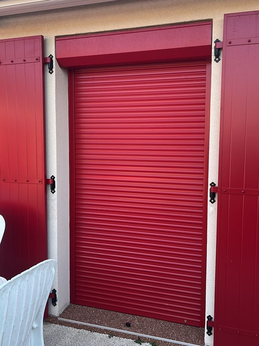 Volet roulant rouge pose sur une porte entre des volets battants assortis